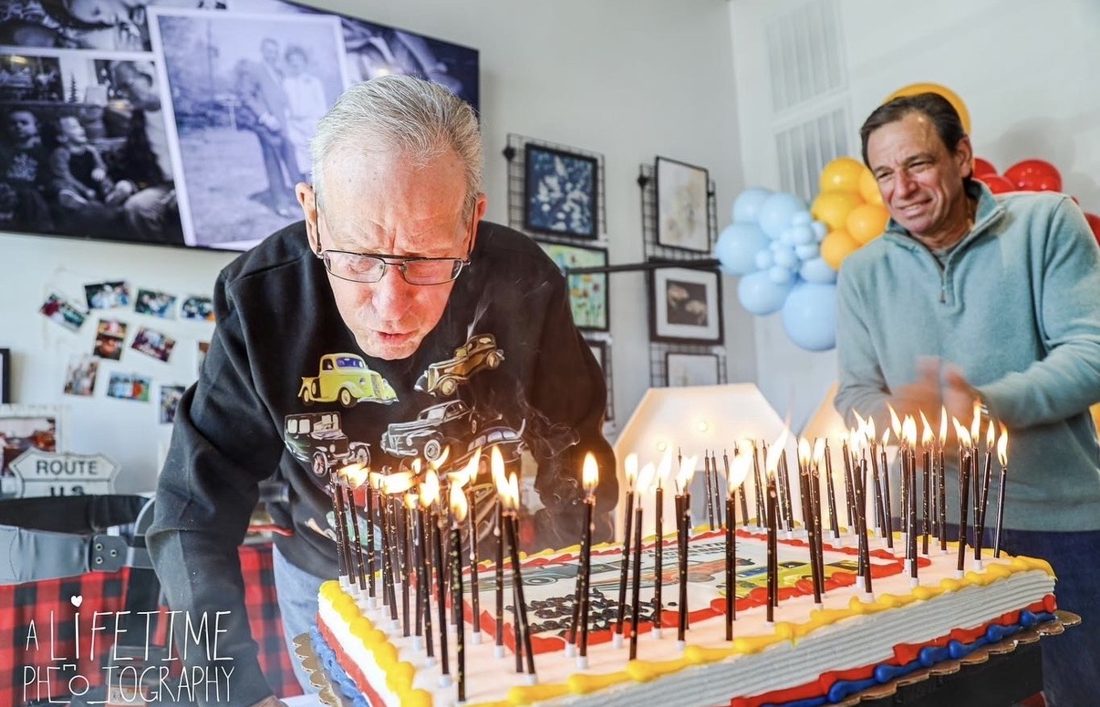 Buddy blowing out a cake full of candles, surrounded by family