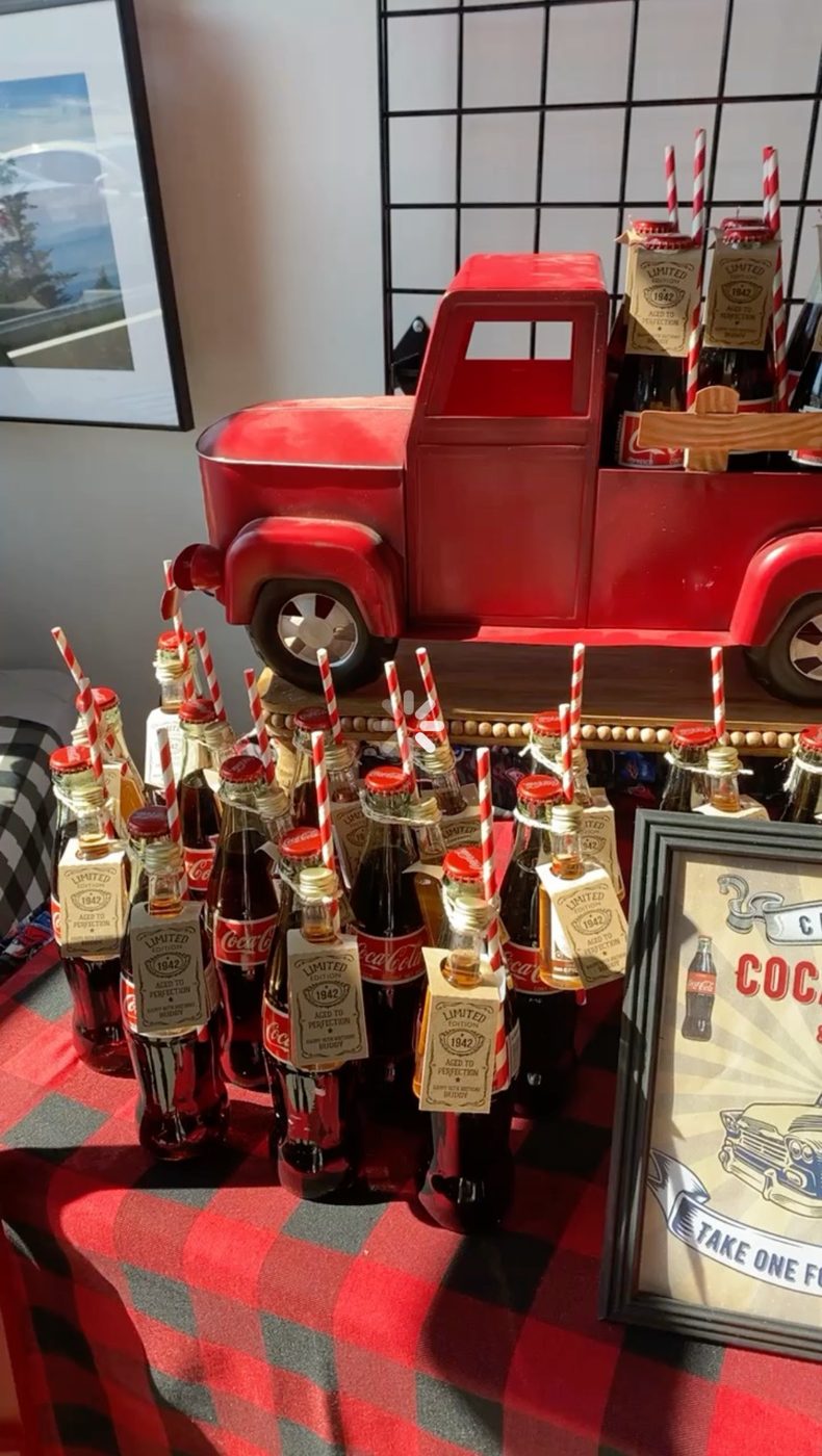 Glass Coca-Cola bottle favors with striped straws and 1942 tags beside a vintage red toy truck