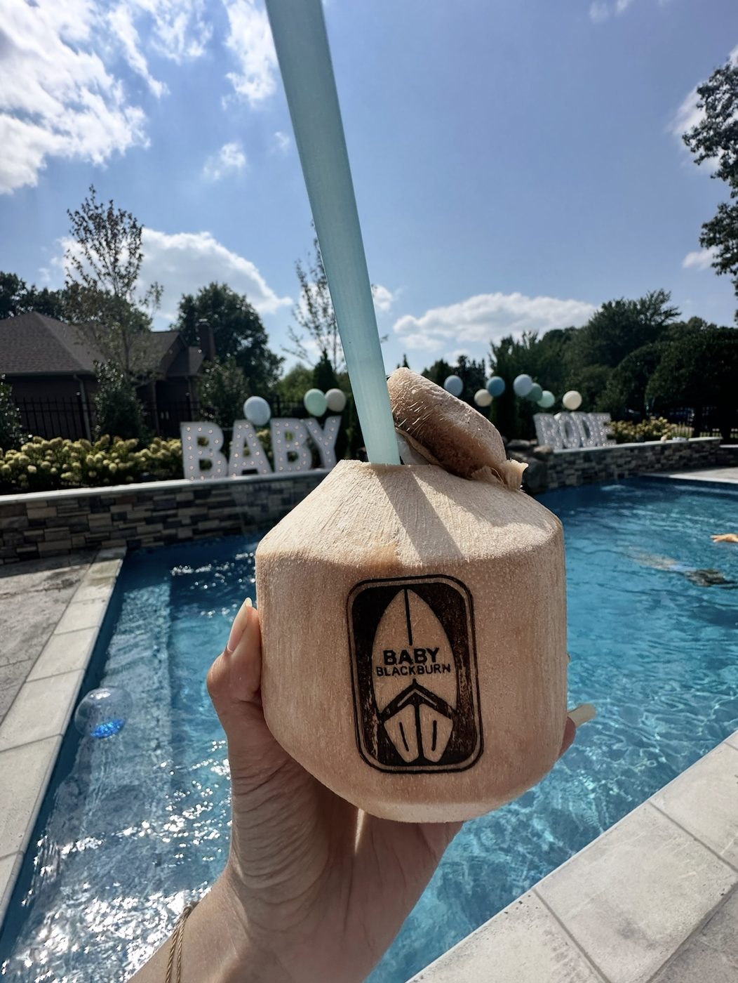 A coconut drink with a surfboard logo held up beside a sparkling pool